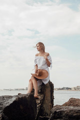 Young woman by the sea. Beautiful girl in white dress and hat on vacation. Travel to the Black Sea.