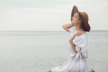 Fototapeta na wymiar Young woman by the sea. Beautiful girl in white dress and hat on vacation. Travel to the Black Sea.