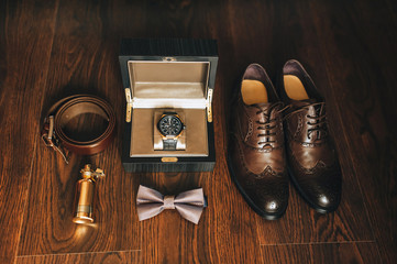Gentleman's set of businessman and groom: shoes, perfume, belt, watch, bow-tie. Wedding details on a wooden background. Photography, concept.