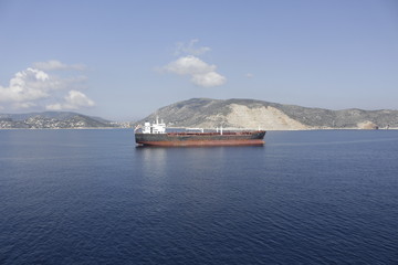 The tanker is anchored off the coast of the island, its hull is covered with rust and the paint has...