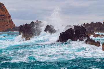 Ocean waves break against coastal cliffs on a cloudy summer day