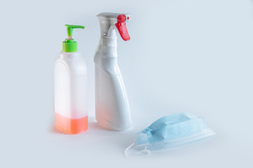 The bottle spray of white color with the red button, a liquid soap and medical mask is on a table of the white color, a set during a pandemic for disinfection, protection of respiratory system