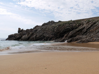 Une plage de sables fin avec la côte rocheuse surplombant la mer