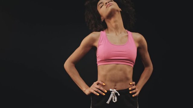 A beautiful young african american woman in sportswear is warming her neck doing exercises isolated over black background
