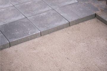 Rows of concrete square pavers or tiles nicely laid in prepared flat sand surface. Still some work...