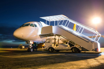 Fototapeta na wymiar White passenger aircraft with boarding stairs at the night airport apron