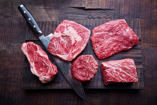 variety of raw beef steaks on a wooden board with a knife, fresh raw meat, copy space, top view