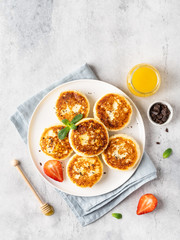 Cottage cheese pancakes, syrniki, ricotta fritters on ceramic plate with honey, chocolate and fresh strawberry. Healthy and delicious morning breakfast.Top view, copy space. Grey concrete background. 