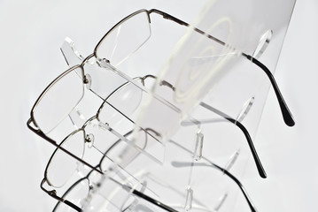 Many glasses on a white background. Glasses are stacked in a row on a transparent shop window. Glass stand on gray table. Sale and exhibition of optics.