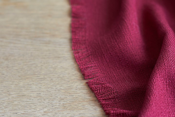 Close-up edge of burgundy tablecloth with fringe on wooden table, selective focus