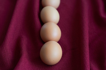 Natural eggs on red tablecloth, several brown chicken eggs lie on burgundy tablecloth, selective focus