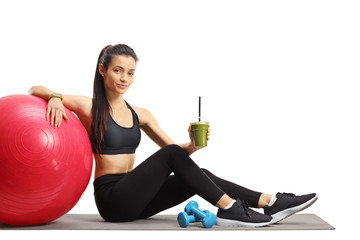 Young female sitting on the floor with a fitness ball and a healthy green smoothie