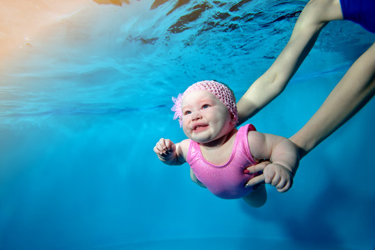 Close-up of a smiling little girl swimming underwater in a children's pool, with her mother supporting her with her arms. Concept. Digital photo. Horizontal orientation.