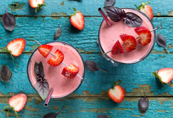 Top view on the strawberry smoothies in a glasses with metal straws, basil leaves, strawberries on cocktail sticks on turquoise wooden surface.