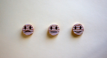 Various emoticons made of wooden circles and hand drawn lines of a mouth. Over yellow background in a conceptual image of quality and feedback.