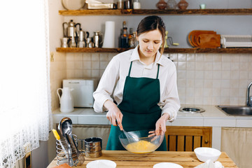 Fototapeta na wymiar A young beautiful girl stands in the kitchen at the table and will baking cake. She is food blogger. Healthy Lifestyle. Cooking At Home. Ketogenic diet and menu