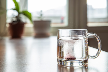 Sparkling tablet throw into a glass transparent glass, the glass is on a table, a pill for cold of...