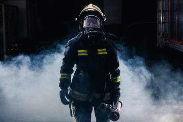 Portrait of a female firefighter wearing a helmet and all safety equipment a while holding a...