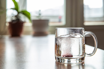 Sparkling tablet throw into a glass transparent glass, the glass is on a table, a pill for cold of...