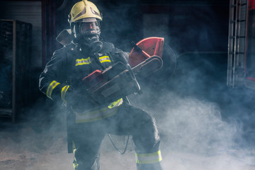 Portrait of a firefighter wearing full protective equipment posing with a chainsaw on his shoulder....