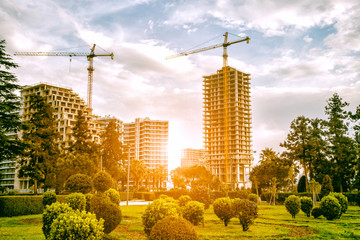 Construction site with green park area. Cranes and buildings in morning sun