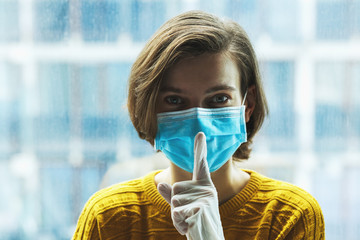 Woman in medical mask with finger near mouth. Panic, silence and calm during coronavirus pandemic concept.