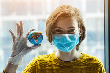 Woman in medical mask holding global earth model in hand in gloves. Global problem of coronavirus pandemic concept.