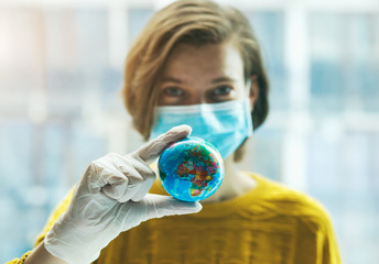 Woman in medical mask holding global earth model in hand in gloves. Global problem of coronavirus pandemic concept.