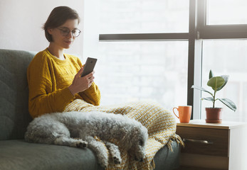 Woman working with phone at home quarantine. Coffee or tea, dog and warm plaid for comfortable workplace. Stay at home campaign.