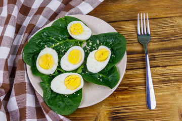 Boiled eggs with fresh spinach leaves and sesame seeds on wooden table. Top view