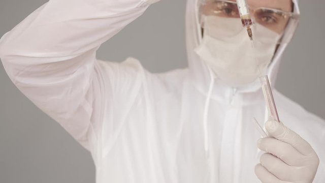 A male researcher is doing research in a laboratory. The scientist is wearing full-covering equipment as he deals with infectious liquid. The man is trying to fing the vaccine for coronairus. He is