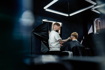 Male haircut with electric razor. Tattooed Barber makes haircut for client at the barber shop by using hairclipper. Man hairdressing with electric shaver.