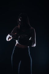 Fototapeta na wymiar Silhouette portrait with dark contrast of a young fitness girl putting on her boxing gloves