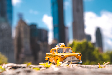 A yellow classic taxi model parked in Central park in New York city on a warm sunny day surrounded...