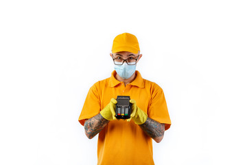 A cautious young man from a courier delivery service in a medical mask and gloves holds a terminal in his hands for cashless payment on a white background