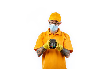 A cautious young man from a courier delivery service in a medical mask and gloves holds a terminal in his hands for cashless payment on a white background