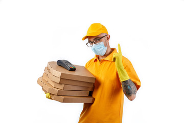 A cautious young man from a courier delivery service in a medical mask and gloves holds boxes with pizza and a terminal for cashless payment on a white background
