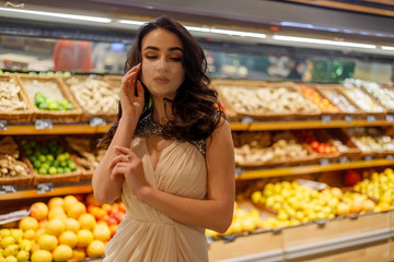 Woman with mask safely shopping groceries amid the coronavirus pandemic in stocked grocery store. brunette buy fruits, vegetables at supermarket. Shortage fresh produce. Woman Evening Sparkling Dress