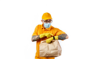 Cautious young man from a courier delivery service in a medical mask and gloves holds a package with an order in his hands and looks at his watch on a white background