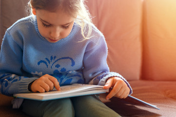 a cute little european kid girl of seven years old reads a book, stay at home during the self isolation of the covid-19 corona virus quarantine. flare