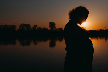 Pretty young pregnant woman with reflection lake in the evening.