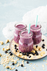 Three blueberry smoothie in small jars with straw on light blue background, vertical format