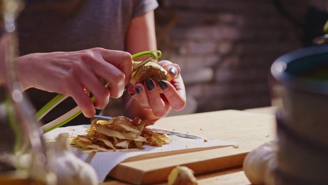 Woman peeling ginger and vegetables for cooking on kitchen table. Closeup hands. Cosy dark room.