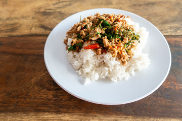 Rice topped with stir-fried pork and basil in a white dish.