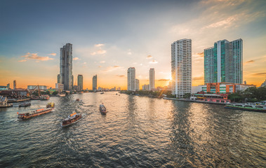 Fototapeta premium Chao Phraya River with Boats and Skyscrapers at Sunset as Seen from Taksin Bridge in Bangkok, Thailand