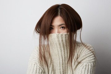 Portrait of beautiful asian woman. Hiding her face in warm sweater .She is catching hair.