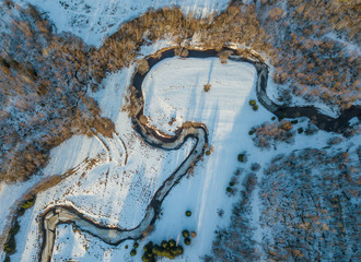 A river flow through a forest and fields under the snow