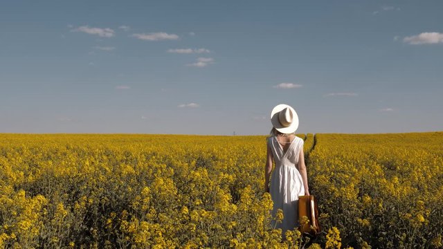 Beautiful woman in dress with suitcase in rapeseed field