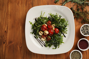 salad of arugula of tomatoes, cherry and mozzarella on a plate on a wooden table (background)
there is a place for text, may be suitable for menu design