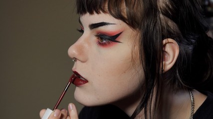 Close up side angle of a goth / punk look teen girl applying dark red lipstick